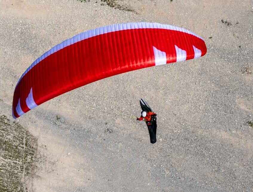Red paraglider glides over rocky terrain in aerial perspective