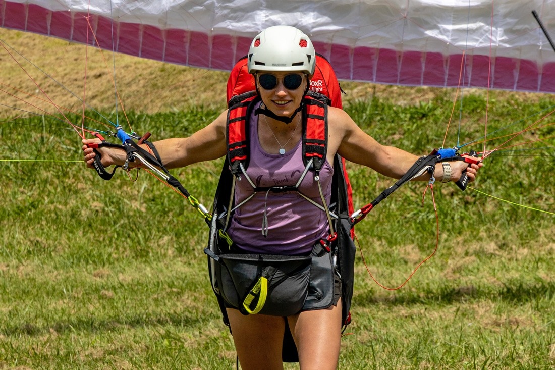 Female paraglider pilot walking with harness after landing